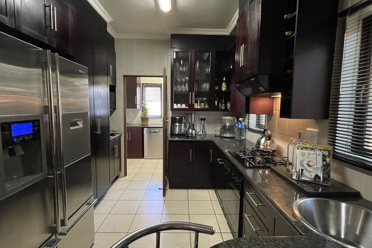 A well-appointed kitchen featuring dark wood cabinetry, granite countertops, a gas hob, and an integrated scullery area with tiled flooring throughout.