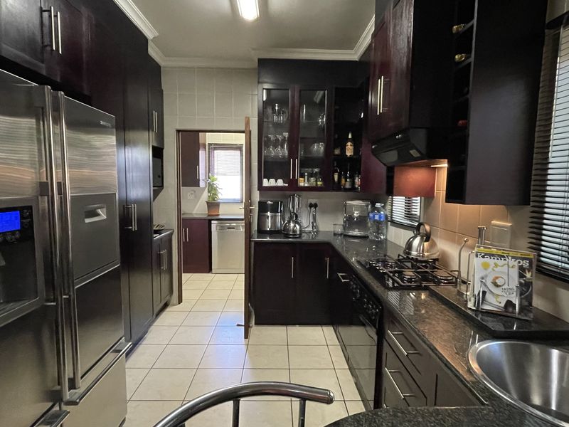 A well-appointed kitchen featuring dark wood cabinetry, granite countertops, a gas hob, and an integrated scullery area with tiled flooring throughout.