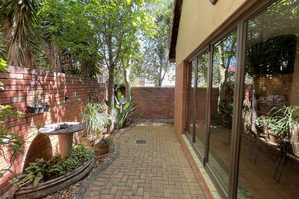 A private rear courtyard featuring a paved walkway, brick boundary walls, and large sliding glass doors providing access to the home.