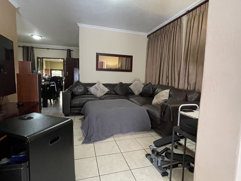 A spacious living room featuring tiled flooring and neutral wall finishes, with an open-plan layout leading into the adjacent dining area.