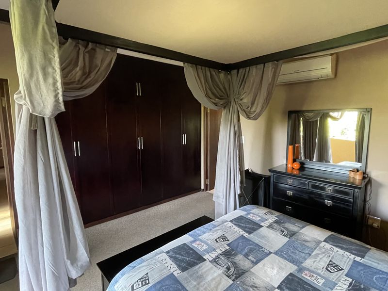 A bedroom featuring dark wood built-in cupboards, carpeted flooring, and a wall-mounted split-system air conditioning unit.