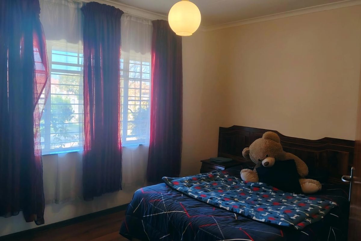 A bedroom featuring wooden flooring, a built-in headboard, and windows fitted with security bars.