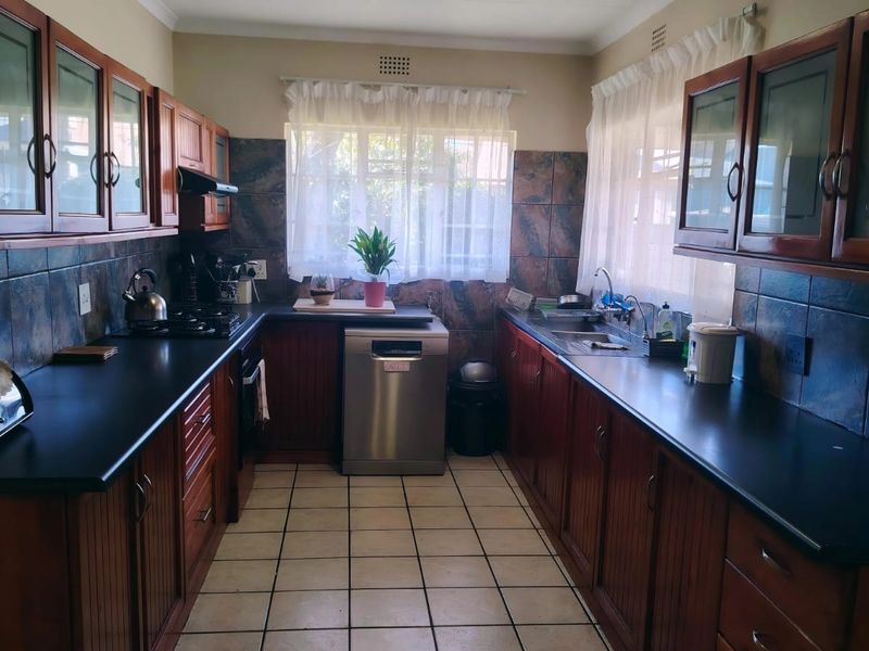 A functional galley-style kitchen featuring warm wooden cabinetry, dark laminate countertops, tiled backsplash, and ceramic floor tiles with ample storage space.