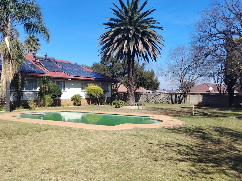 Spacious rear garden featuring a swimming pool, established trees, and a house roof equipped with solar panels and a solar water heating system.