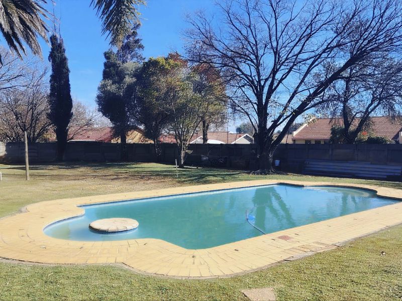 Spacious backyard featuring a swimming pool with paved surround, enclosed by a perimeter wall and mature trees.