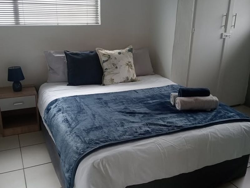 A functional bedroom featuring tiled flooring, a built-in wardrobe, and venetian blinds, providing a clean and practical living space.