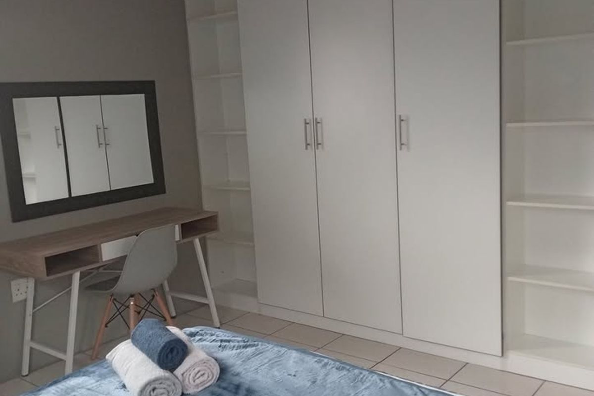 A well-maintained bedroom featuring extensive built-in cupboards and integrated shelving units, complemented by neutral tiled flooring.