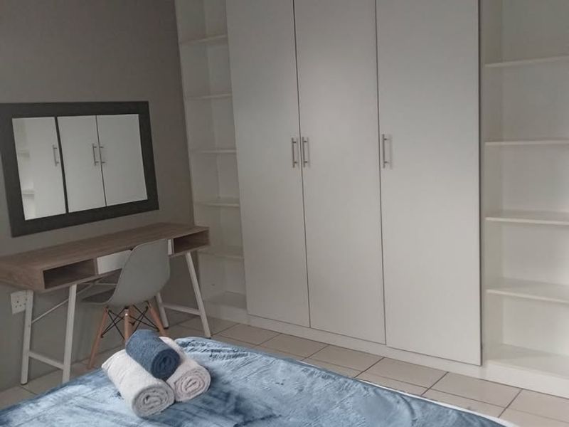 A well-maintained bedroom featuring extensive built-in cupboards and integrated shelving units, complemented by neutral tiled flooring.