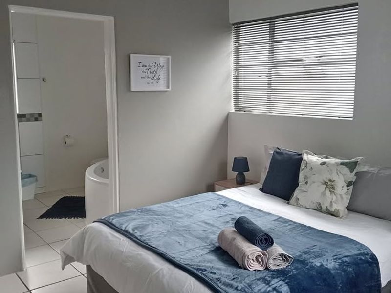 A well-maintained bedroom featuring tiled flooring, neutral wall tones, and direct access to an en-suite bathroom with a corner bath.