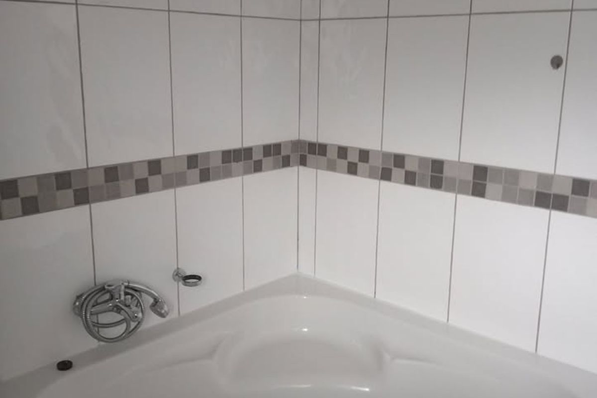 A corner bathtub in a tiled bathroom, currently missing some fixtures and hardware, offering potential for a modern renovation.