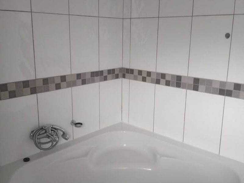 A corner bathtub in a tiled bathroom, currently missing some fixtures and hardware, offering potential for a modern renovation.