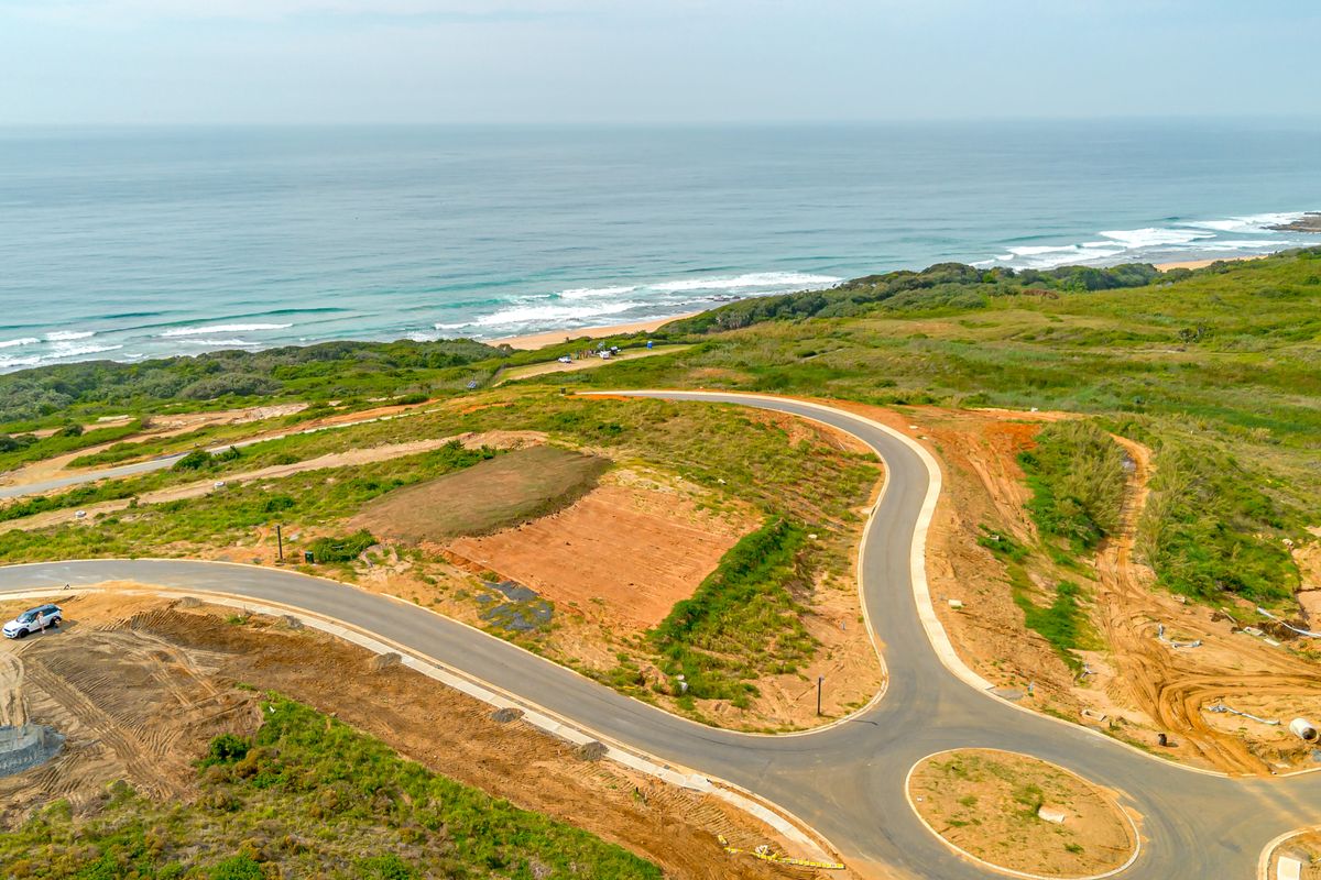 Aerial view of a residential development site featuring paved roads, a roundabout, and direct proximity to the coastline.