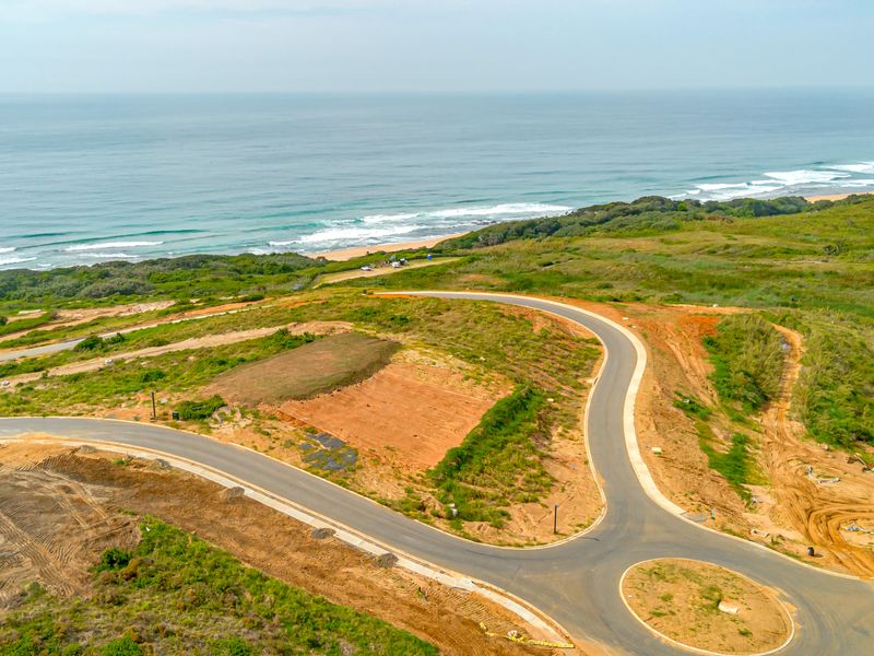 Aerial view of a residential development site featuring paved roads, a roundabout, and direct proximity to the coastline.
