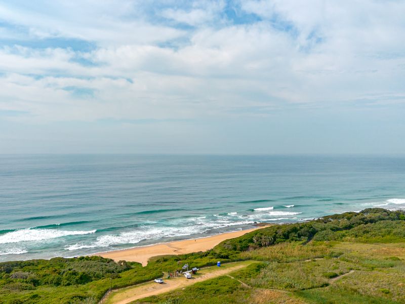 An aerial view of the coastal property, showcasing direct beach access, natural vegetation, and expansive ocean views.