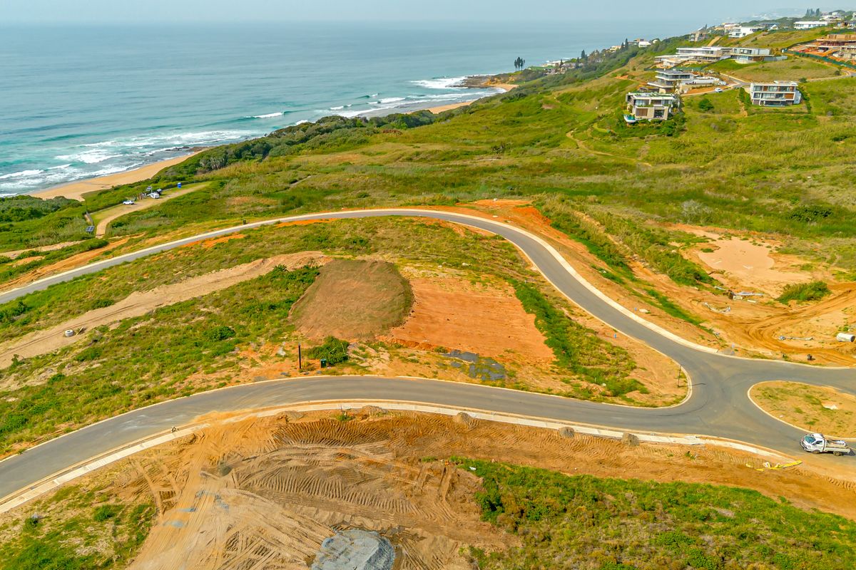 Aerial view of a vacant residential plot featuring paved road access and scenic coastal views in a developing estate.