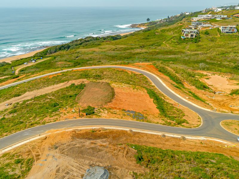 Aerial view of a vacant residential plot featuring paved road access and scenic coastal views in a developing estate.