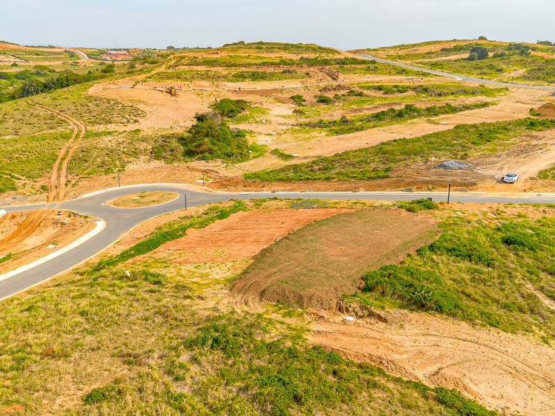 Aerial view of an undeveloped residential estate featuring paved roads, a roundabout, and cleared plots ready for construction.