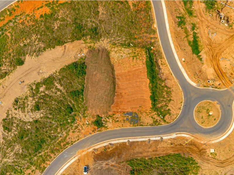 An aerial view of a vacant residential plot situated within a developing estate, featuring access to paved roads and a nearby roundabout.