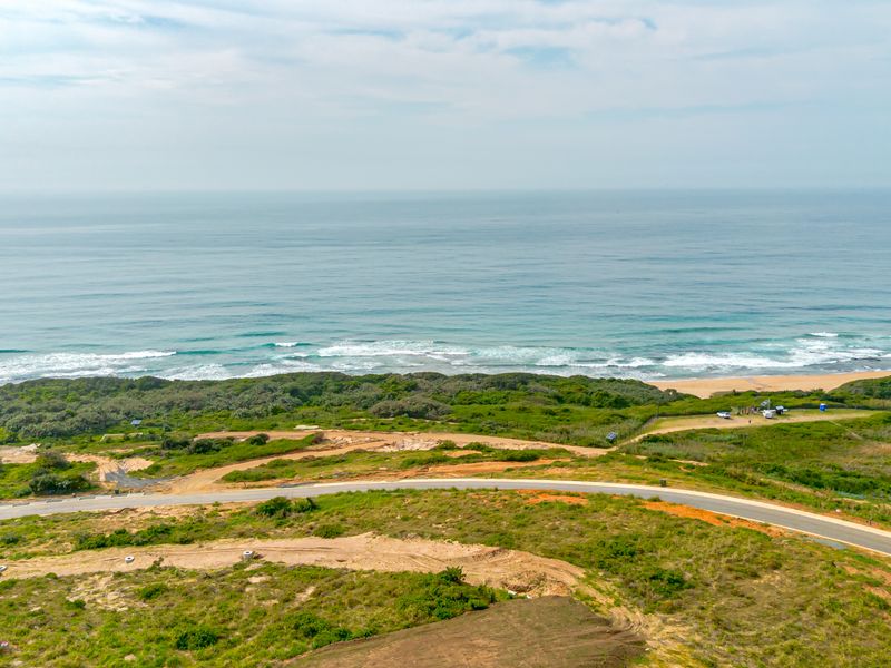 Aerial view of vacant residential land featuring coastal proximity, natural vegetation, and established paved road access.