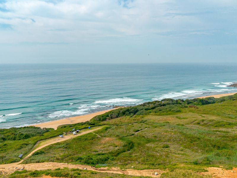Aerial view of a coastal residential land plot featuring natural vegetation, an unpaved access track, and direct proximity to the ocean shoreline.