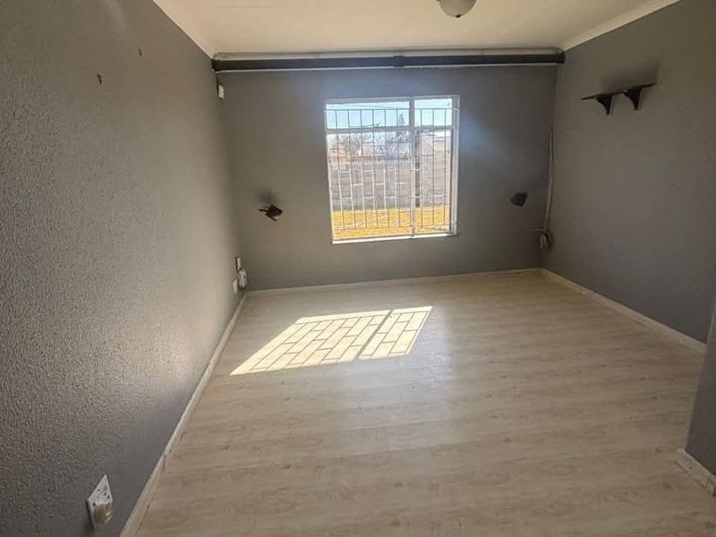 An empty bedroom featuring light-toned laminate flooring, grey painted walls, and a window fitted with security bars.