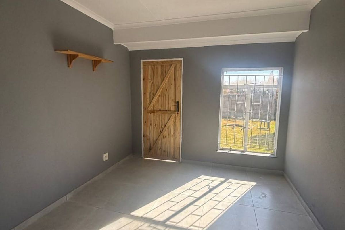 A vacant bedroom featuring tiled flooring, a wooden door, and a window fitted with security bars, offering a neutral canvas for personalization.