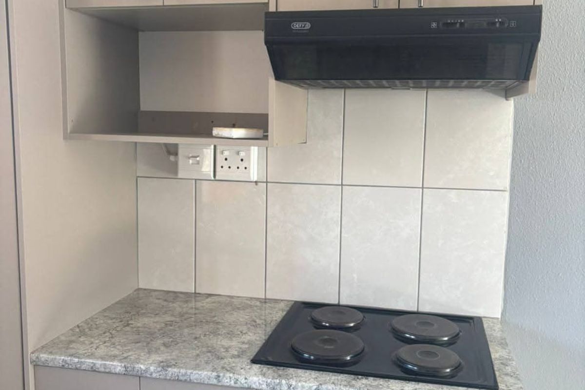 A compact kitchen area featuring built-in cabinetry, a laminate countertop, an electric hob, a built-in oven, and an extractor fan with tiled splashback.