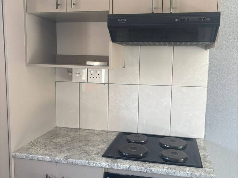 A compact kitchen area featuring built-in cabinetry, a laminate countertop, an electric hob, a built-in oven, and an extractor fan with tiled splashback.