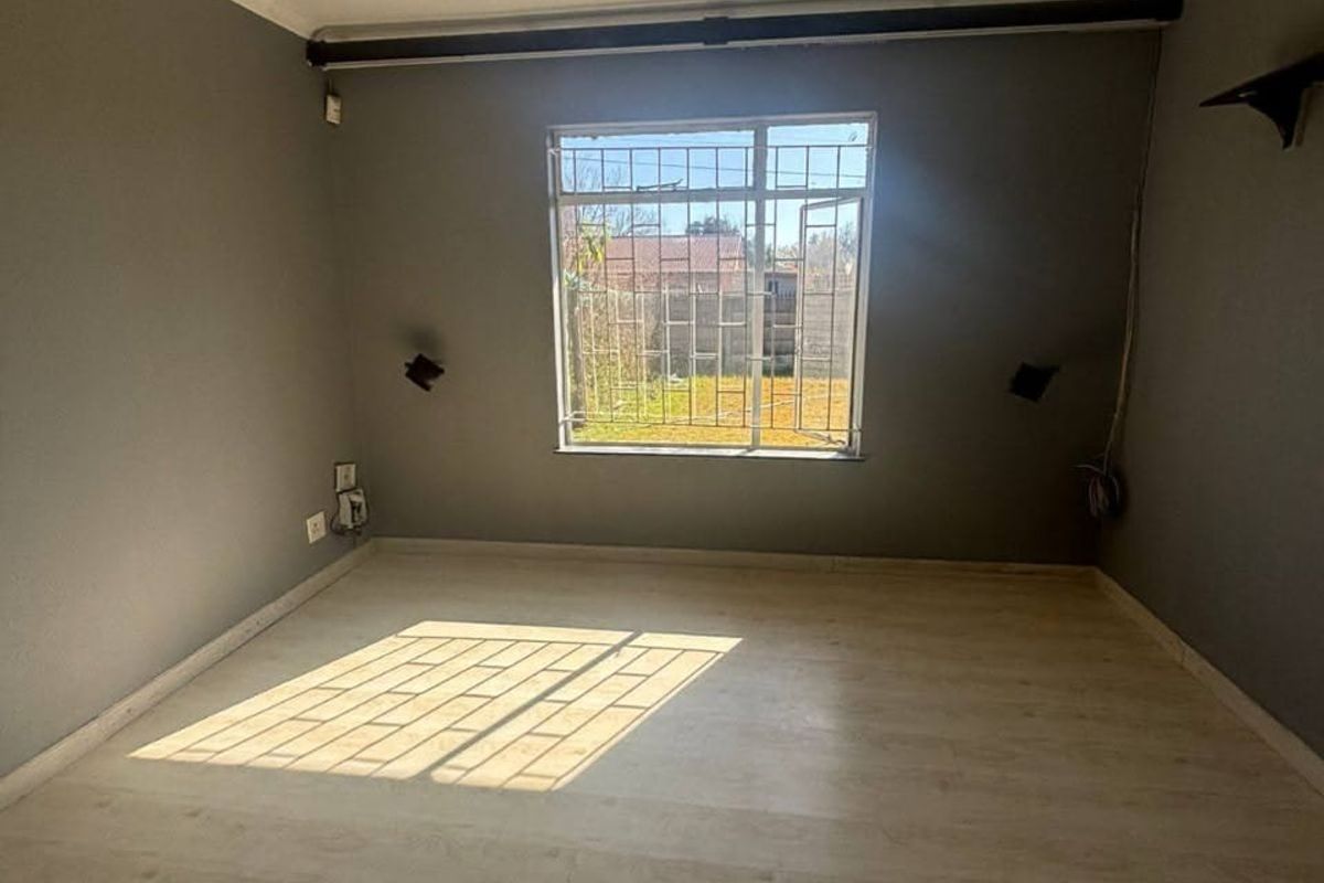 An empty bedroom featuring laminate flooring, grey walls, and a window fitted with security bars, offering a blank canvas for personalization.