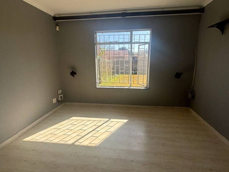 An empty bedroom featuring laminate flooring, grey walls, and a window fitted with security bars, offering a blank canvas for personalization.