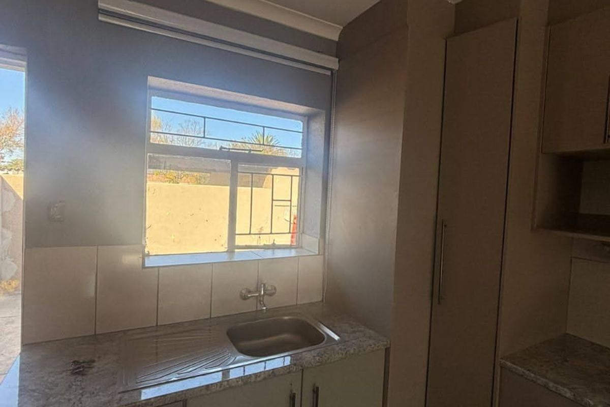 A functional kitchen area featuring built-in cabinetry, laminate countertops, and a stainless steel sink with a tiled backsplash.