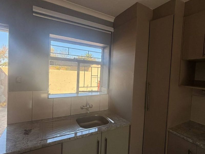 A functional kitchen area featuring built-in cabinetry, laminate countertops, and a stainless steel sink with a tiled backsplash.