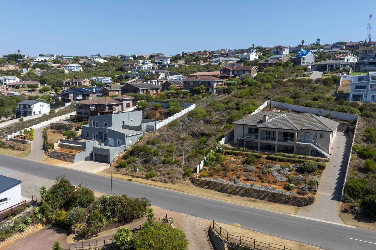 Aerial view of a residential neighborhood featuring vacant land plots, paved roads, and established surrounding homes in a coastal hillside setting.