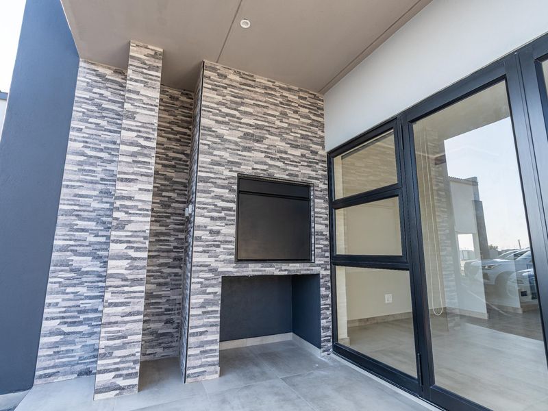 A modern covered patio featuring stone-clad walls, a built-in braai, and large aluminium sliding doors providing seamless access to the interior living space.