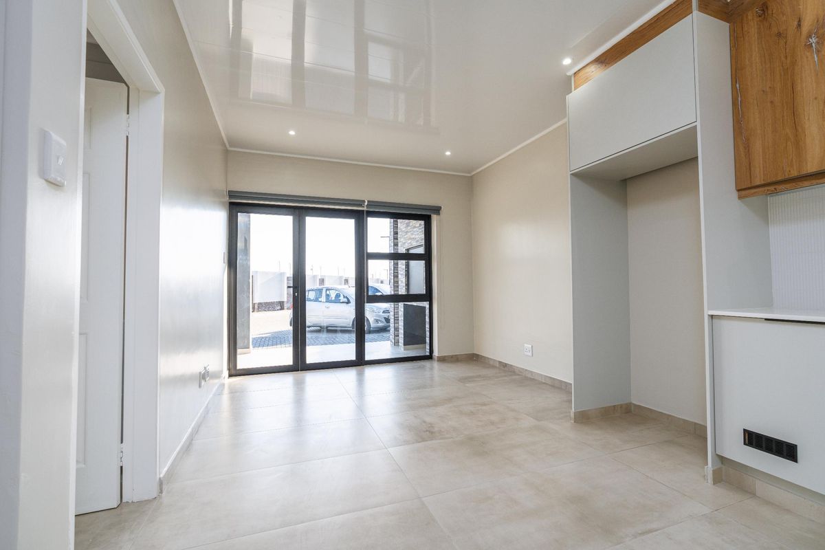 Modern open-plan living area featuring large format floor tiles, a high-gloss ceiling with recessed lighting, and sliding glass doors leading to the exterior.