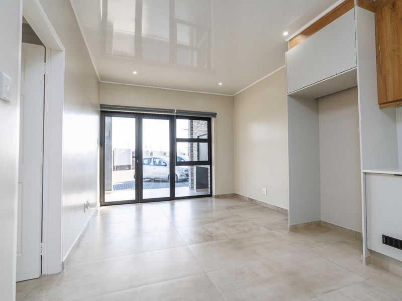 Modern open-plan living area featuring large format floor tiles, a high-gloss ceiling with recessed lighting, and sliding glass doors leading to the exterior.
