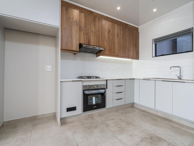 Modern kitchen featuring wood-look upper cabinets, sleek white lower cabinetry, built-in oven, gas hob, and tiled flooring in a clean, contemporary finish.