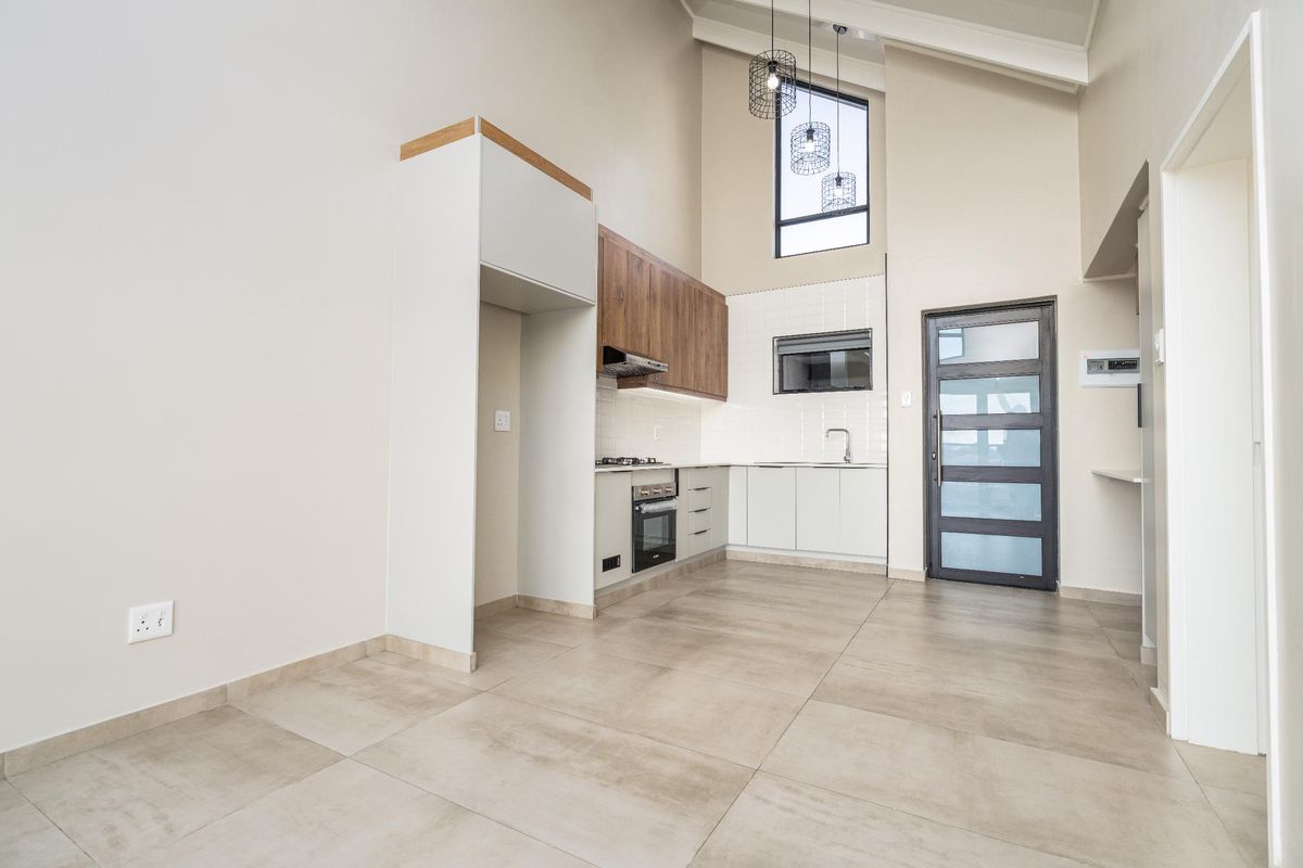 Modern kitchen featuring high vaulted ceilings, sleek cabinetry, built-in appliances, and large format floor tiles in an open-plan layout.