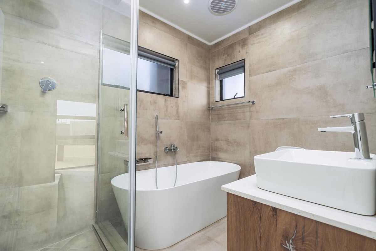 Modern bathroom featuring a sleek freestanding bathtub, glass-enclosed shower, vessel sink on a wood-finish vanity, and neutral large-format wall tiles.