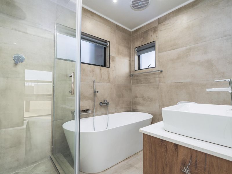 Modern bathroom featuring a sleek freestanding bathtub, glass-enclosed shower, vessel sink on a wood-finish vanity, and neutral large-format wall tiles.