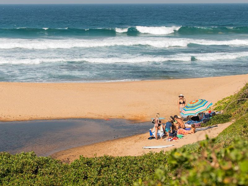 A scenic view of the coastline featuring a sandy beach, natural estuary, and ocean waves.