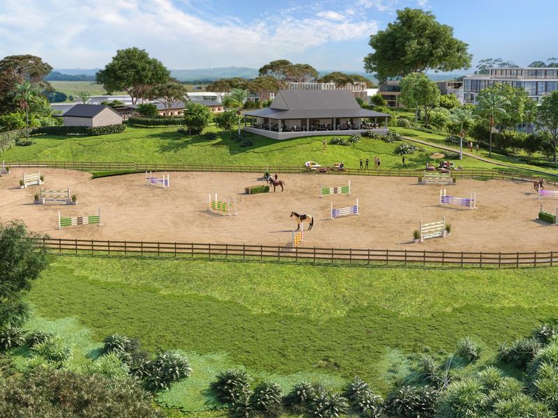 An aerial view of a professional equestrian arena featuring post and rail fencing, set within a landscaped estate with a clubhouse.