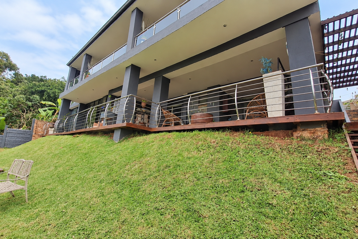 A multi-level rear exterior view featuring timber decking, stainless steel balustrades, and a pergola, overlooking a landscaped garden with a timber staircase.