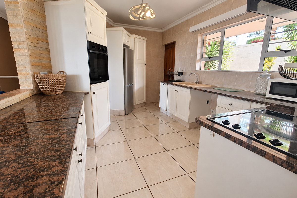 A functional kitchen featuring granite countertops, built-in oven, ceramic hob, and tiled finishes, offering a clean and well-maintained workspace.