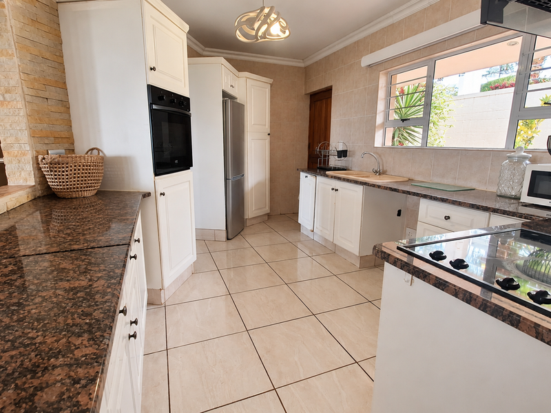 A functional kitchen featuring granite countertops, built-in oven, ceramic hob, and tiled finishes, offering a clean and well-maintained workspace.
