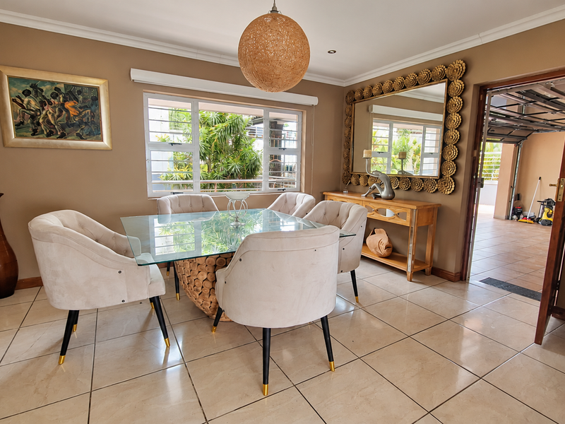 A well-maintained dining room featuring tiled flooring, recessed lighting, and a window with security bars, providing a bright and functional space for meals.