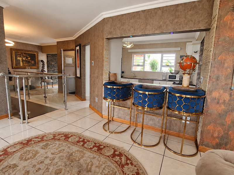 An open-plan living area featuring tiled floors, a stainless steel balustrade, and a pass-through window connecting to the kitchen space.