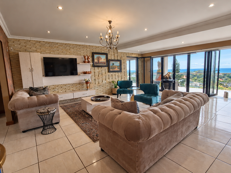 Spacious living room featuring a textured stone accent wall, tiled floors, and large bi-fold doors opening to a scenic coastal view.
