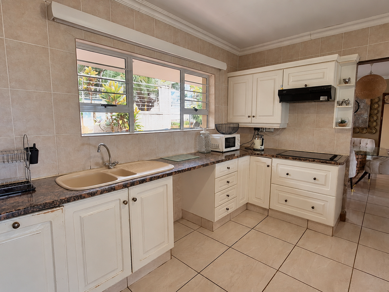 A functional kitchen featuring cream cabinetry, granite countertops, ceramic tiling, and an integrated extractor fan, offering a classic layout with ample storage space.