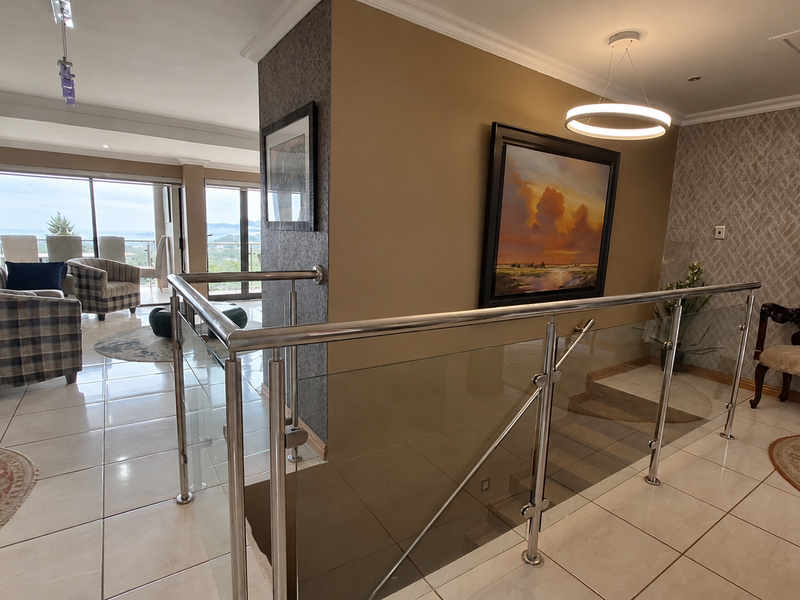 Spacious landing area featuring a modern stainless steel and glass balustrade, tiled flooring, and elegant textured wallpaper with recessed and pendant lighting.